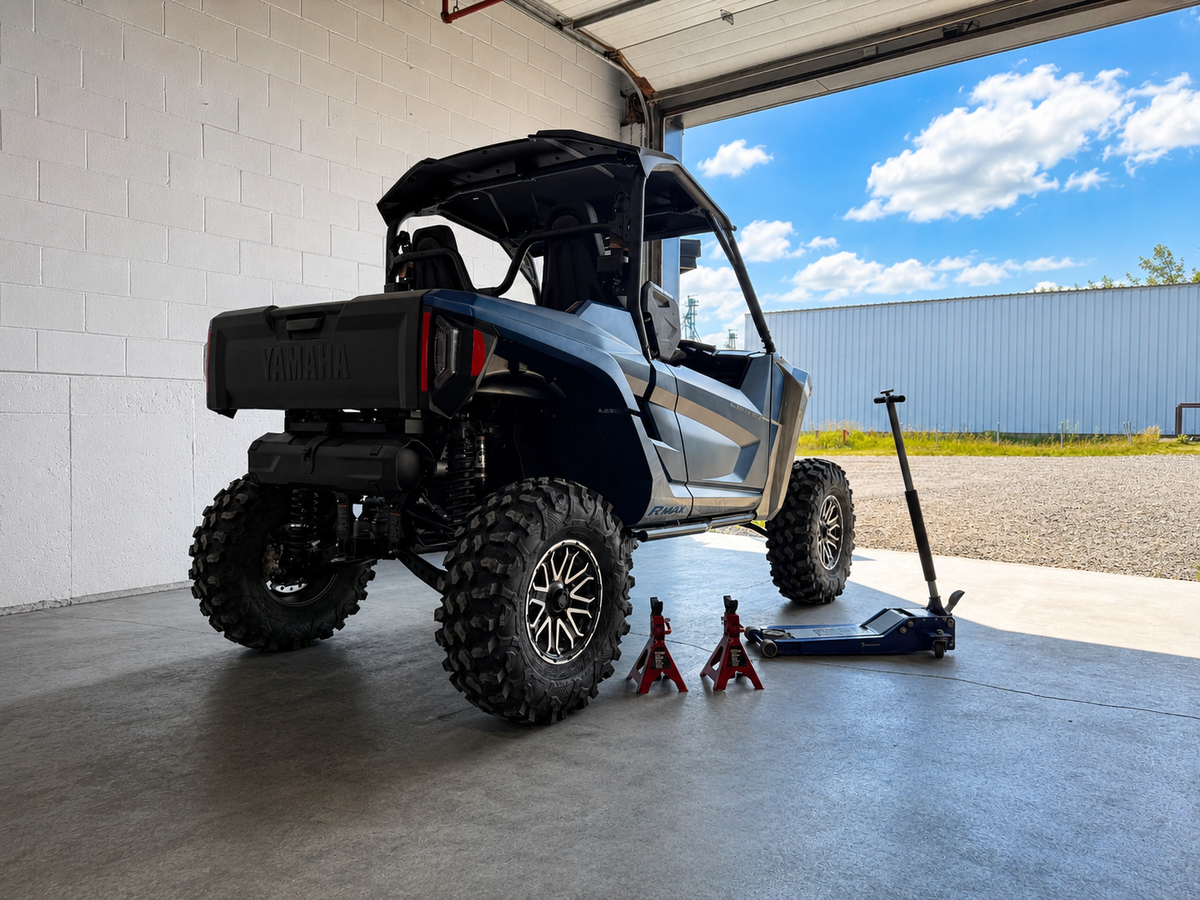 Yamaha RMAX UTV parked on a level concrete surface with a floor jack and jack stands ready for wheel spacer installation.