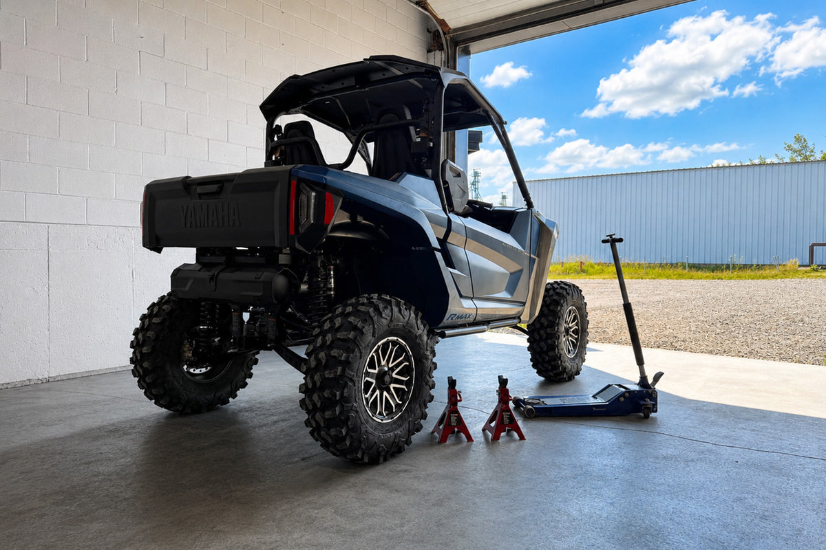 Yamaha RMAX UTV parked on a level concrete surface with a floor jack and jack stands ready for wheel spacer installation.