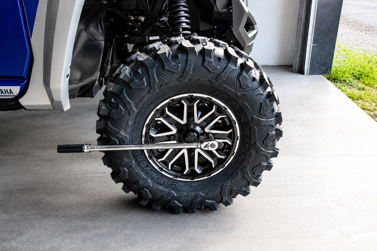 Loosening ATV or UTV wheel lug nuts with a torque wrench before lifting the vehicle for wheel spacer installation.